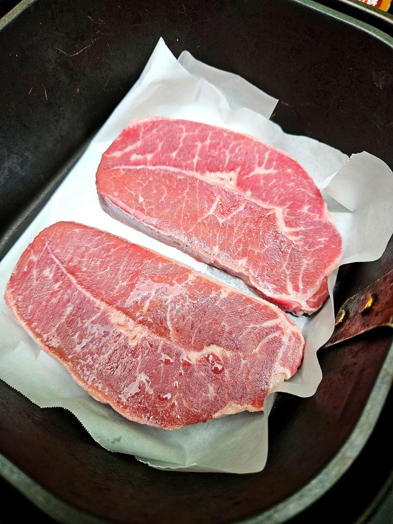 Placing seasoned flat iron steak into the preheated air fryer basket Putting steak in air fryer
