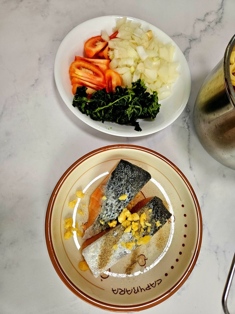 Dicing onion, tomatoes, garlic and seasoning the salmon fillet with salt, white pepper and garlic Cutting vegetables and seasoning salmon