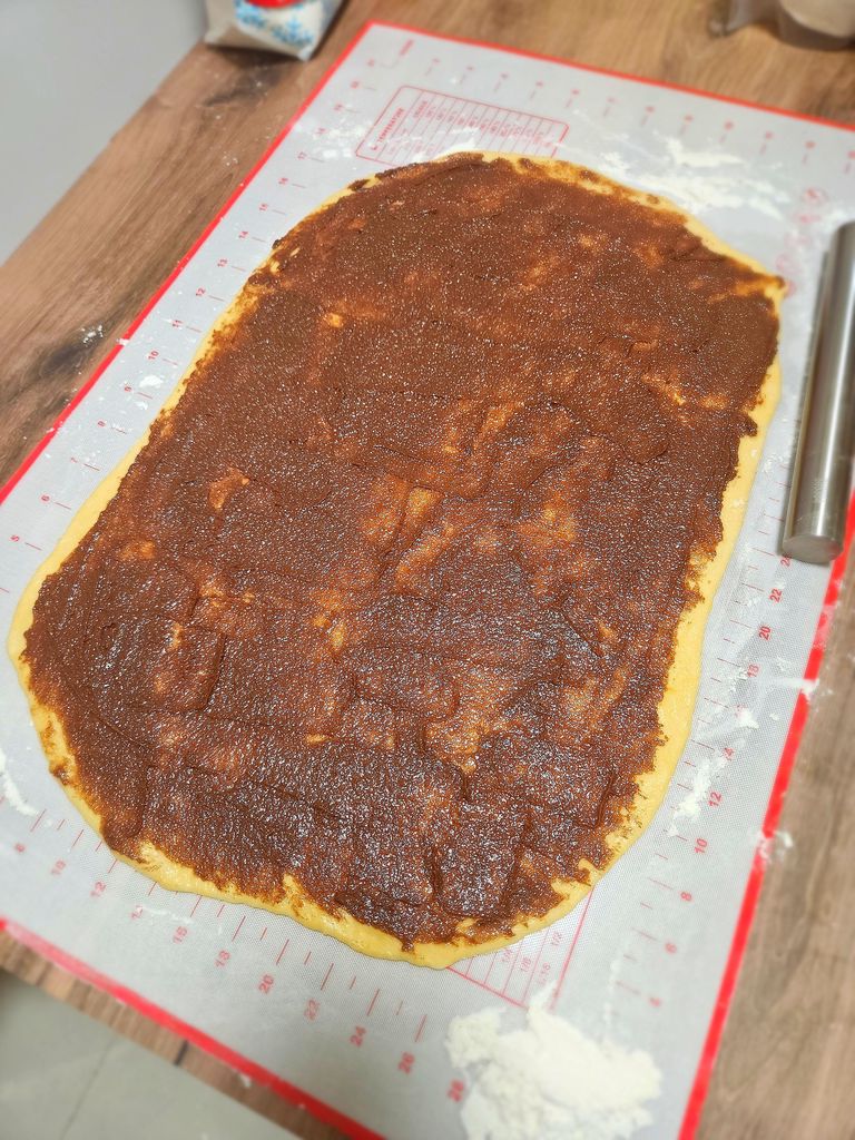 Evenly spreading the cinnamon filling over the rolled dough.