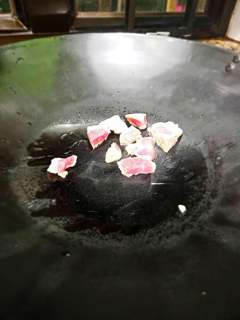 Adding the pork to a hot wok with oil
